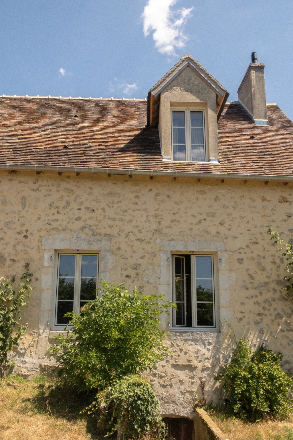 La façade en pierre de la maison d'hôtes, sa lucarne et son toit de tuiles anciennes